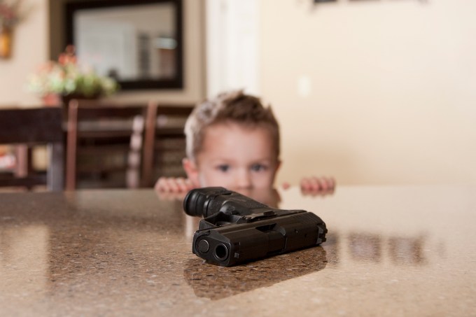 A small child staring at a hand gun within reach on a table